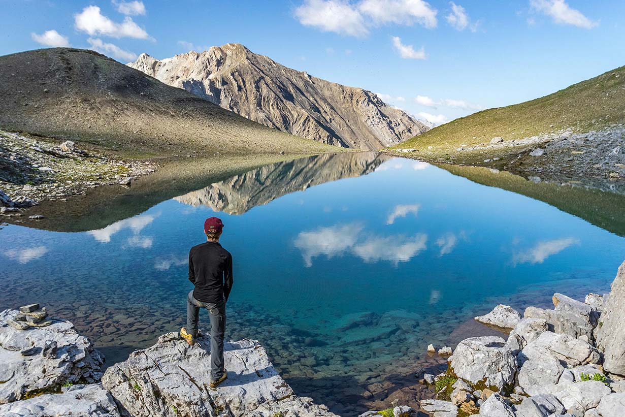 Hiker standing by alpine lake with mountain reflection