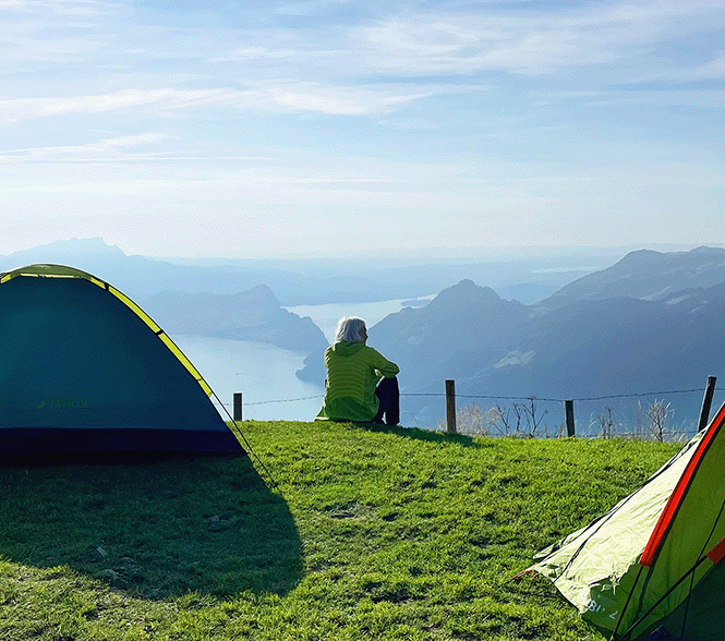 Person sitting by tents overlooking mountain lake