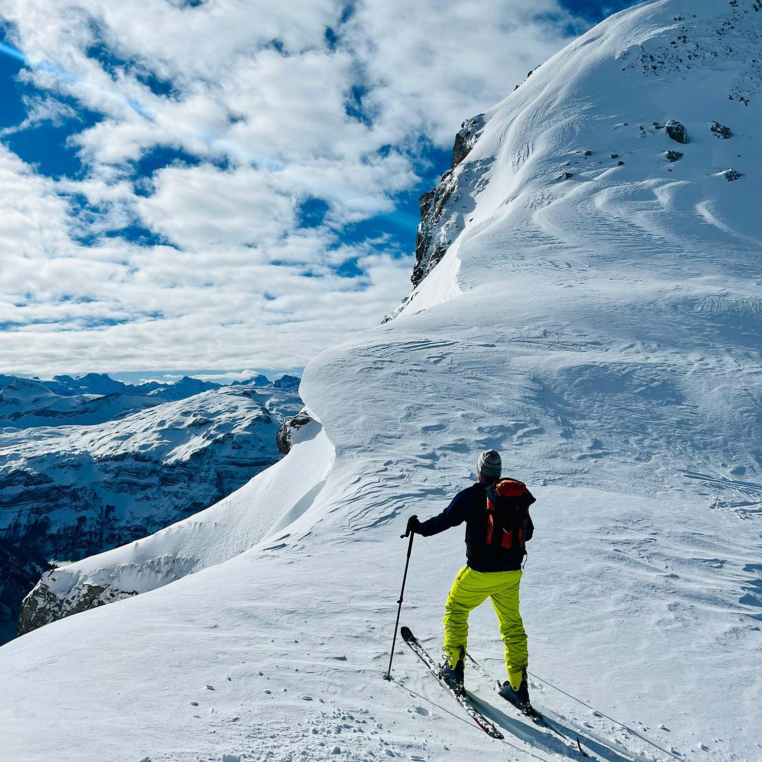 Skier on snowy mountain ridge under cloudy sky